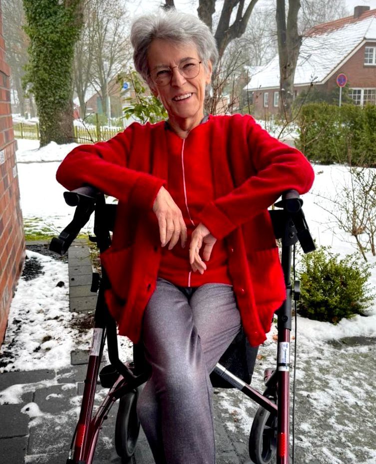 Pflege Leer Eine ältere Frau in einem Rollstuhl trägt einen roten Pullover und sitzt draußen im Schnee.