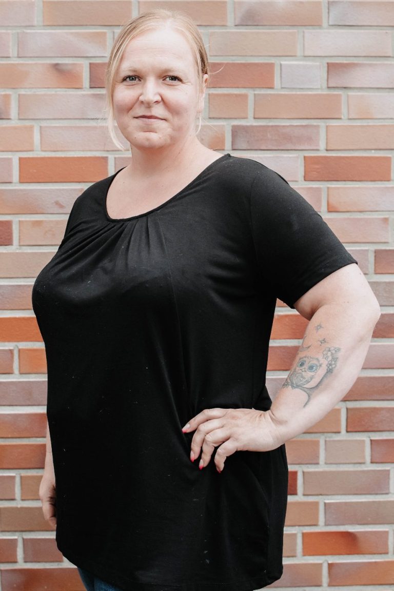 Mann mit verschränkten Armen, lächelnd vor einer Backsteinmauer.