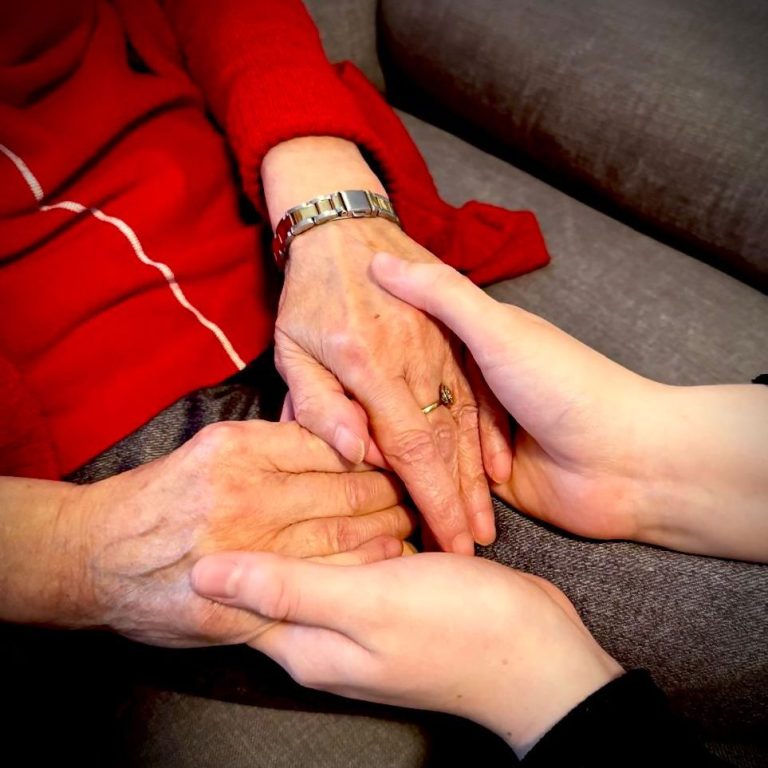 Hände einer älteren Person und einer jüngeren Person, die sich berühren.